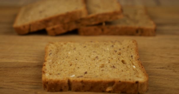 バターは木製のまな板の上に多粒パンの上にナイフで広げられています — ストック動画