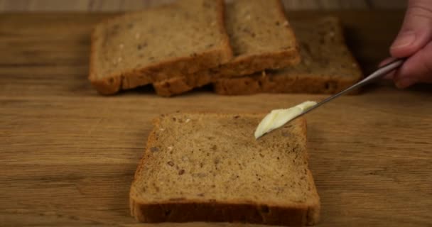 バターは木製のまな板の上に多粒パンの上にナイフで広げられています — ストック動画