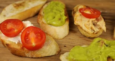 Humus, guacamole ve krem peynir üzerine taze domates ve kızarmış ekmek. Tahta kesme tahtasında çeşitli atıştırmalıklar. Vejetaryenler için yiyecek..