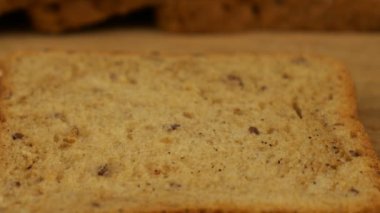 Krem peynir, tahta kesme tahtasındaki çoklu tahıllı ekmeğe bıçak ile sürülmüş..