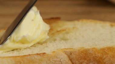 Tereyağı, tahta kesme tahtasındaki kızarmış buğday ekmeğine bıçak ile sürülmüş..