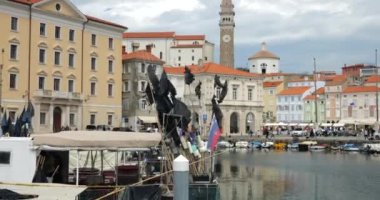 Slovenya bayrağını dalgalandıran ve Piran limanında şehir meydanı ve çan kulesine karşı siyah bayraklı bir tekne..