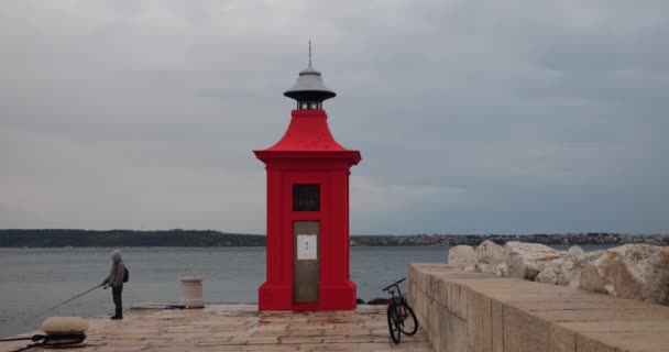 スロベニアの赤灯台近くのピラン港桟橋のロッドを持つ漁師釣り — ストック動画