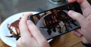 Kız, kafeteryada Tiramisu tatlısının fotoğrafını çekmek için akıllı telefondan bir açı seçiyor..