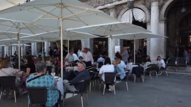 Turistler, Venedik, Piazza San Marco 'daki Procuratie Nuove' da bulunan Florian Kafe 'de dinleniyorlar. İtalya.