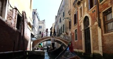 İtalya 'nın Venedik kentindeki birçok kanal köprüsünden birinin altında turist taşıyan bir gondol yüzüyor..