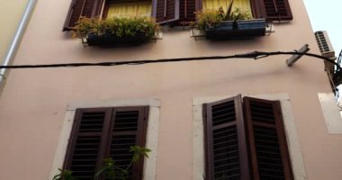 Pencereleri panjurlu ve pencerelerinin altında saksılarda çiçekler olan eski bir Akdeniz kasabasının geleneksel evleri. Aşağıdan yukarıya bak.