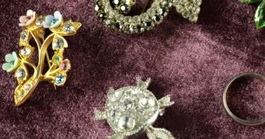 Eski mücevherlerle birlikte kadife kaplama vitrin: Broşlar ve yüzükler. Altın ve gümüş renkli mücevherler, çok renkli kristaller ve metal tanecikleri var..
