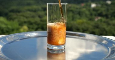 Kola, yeşil bir yaz ormanının arka planına portakal suyundan gelen buzla doldurulur. Yavaş çekim.