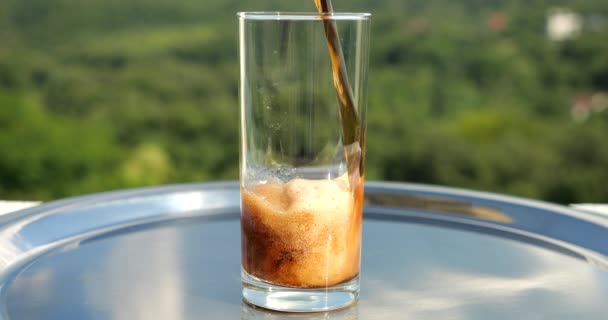 可乐被倒入一个装有冰块的杯子中 背景是一片绿色的夏季森林 慢动作 — 图库视频影像