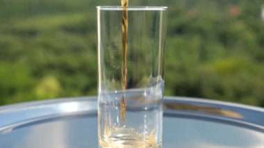 Kola, yeşil bir yaz ormanının arka planında buzlu bir bardağa dökülür. Yavaş çekim.