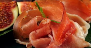 Siyah taş servis tahtasında incir, jambon ve ıspanak yaprakları. Atıştırmalıklar.