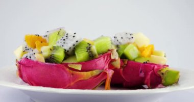 Sağlıklı diyet meyve salatası beyaz arka planda izole edilmiş bir tabakta ejderha meyvesinin deri kasesinde. Bir dilim portakal, kivi, elma..