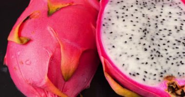 İki yarısı ejderha meyveli pitahaya siyah taşlı servis tahtasının üzerinde..