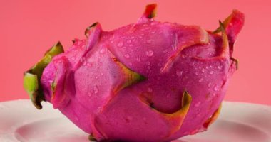 Ejderha meyveli pitahaya, bir tabakta su damlası içinde, pembe arka planda izole edilmiş..