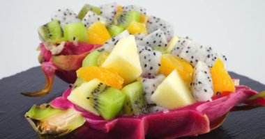 Sağlıklı diyet meyve salatası beyaz arka planda izole edilmiş siyah bir taş servis tahtasındaki ejderha meyvesinin deri kasesinde. Bir dilim portakal, kivi, elma..