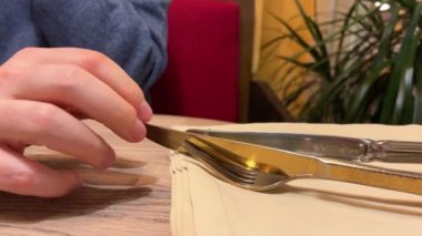 Bir adam restoranda sohbet ediyor. Bir adamın eli ve parmakları çatal bıçak takımının yanında..
