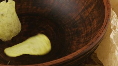 Patates cipsleri arka plandaki mutfak parşömeninde seramik kaseye düşüyor. Yavaş çekim.