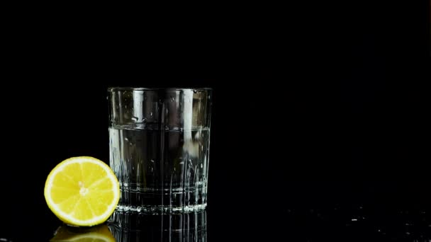 Шматочок Лимона Падає Склянку Води Повільний Рух Ізольовані Чорному Тлі — стокове відео