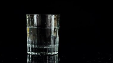 Buz küpleri siyah zemin üzerinde bir bardak suya düşüyor. Ağır çekim. Siyah arkaplanda izole.