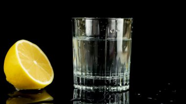Bir dilim limon bir bardak suya düşer. Ağır çekim. Siyah arkaplanda izole.