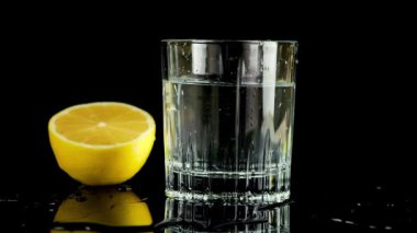 Bir dilim limon bir bardak suya düşer. Ağır çekim. Siyah arkaplanda izole.