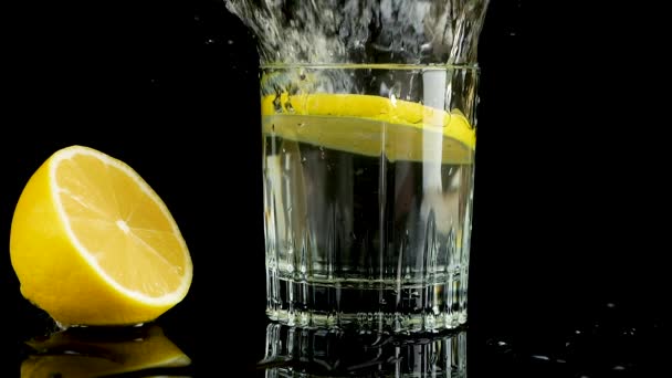 Шматочок Лимона Падає Склянку Води Повільний Рух Ізольовані Чорному Тлі — стокове відео
