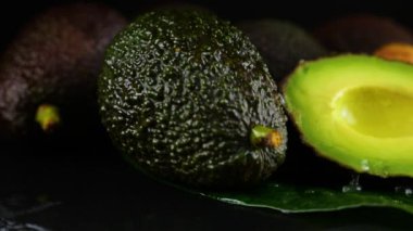 Avokado meyvelerinin üzerine siyah arka planda yapraklarla su damlaları düşer. Çiğ meyve, sağlıklı yiyecek..