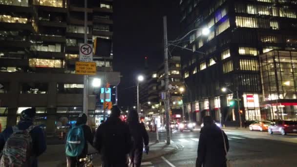 トロント カナダ February 2024 人々のグループは歩行者の交差点で通りを横断します 高層ビルと都市建築の様子 トロントのダウンタウンの夜の通りを歩く — ストック動画