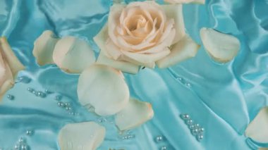Beyaz ve pembe güllerin çiçekleri ve taç yaprakları suyun yüzeyinde süzülür mavi ipek arka planda su altında incilerle birlikte..