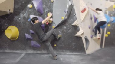 Jimnastik salonunda Asyalı dağcı, kaya duvarına tırmanıyor. İçerde eğlenceli aktif spor egzersizleri..