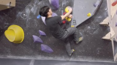 Jimnastik salonunda Asyalı dağcı, kaya duvarına tırmanıyor. İçerde eğlenceli aktif spor egzersizleri..
