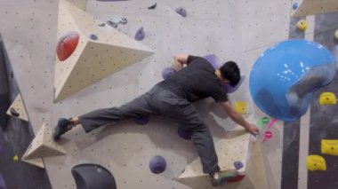 Jimnastik salonunda Asyalı dağcı, kaya duvarına tırmanıyor. İçerde eğlenceli aktif spor egzersizleri..