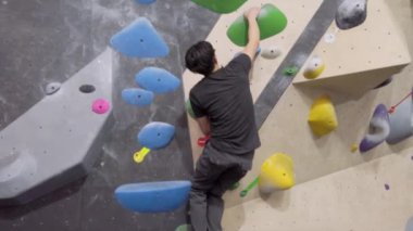 Jimnastik salonunda Asyalı dağcı, kaya duvarına tırmanıyor. İçerde eğlenceli aktif spor egzersizleri..