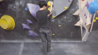 Jimnastik salonunda Asyalı dağcı, kaya duvarına tırmanıyor. İçerde eğlenceli aktif spor egzersizleri..