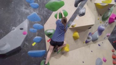 Genç dağcı kız spor salonunda kaya duvarına tırmanıyor..