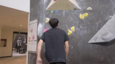 Jimnastik salonunda Asyalı dağcı, kaya duvarına tırmanıyor. İçerde eğlenceli aktif spor egzersizleri..