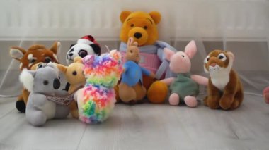 Doldurulmuş ve pofuduk peluş peluş ve gökkuşağı oyuncakları koyunlar, tek boynuzlu at ve koala oyun sahasındaki lamine zemine diğer oyuncakların arka planına düşerler. Yavaş çekim.