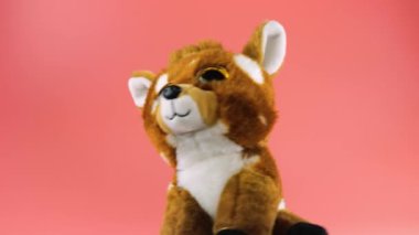 Doldurulmuş ve pofuduk oyuncak geyik yavrusu döner ve pembe bir arka plana bakar..