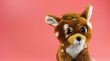 Doldurulmuş ve pofuduk oyuncak geyik pembe arka planda selamlaşır.