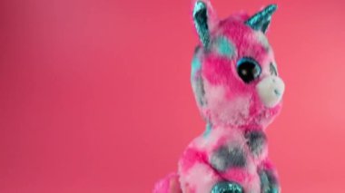 Doldurulmuş ve pofuduk oyuncak pembe tek boynuzlu at pembe arka planda oynuyor ve dans ediyor..
