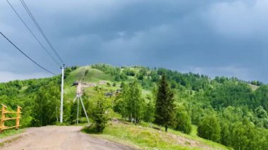 Bir dağ sırası boyunca yol ve fırtınalı bir gökyüzünün altında elektrik hattı. Gökte fırtına ve yağmur bulutları.