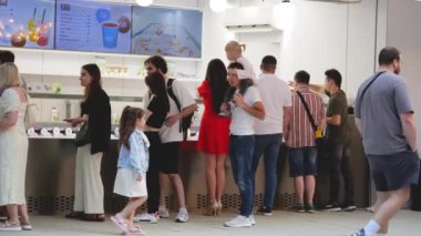LVIV, UKRAINE - 10 Temmuz 2024: Kırmızı elbiseli muhteşem bir esmer kız diğer insanlar ve çocuklar arasında bir sokak kafesinde dondurma satın alır.