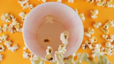 Patlamış mısır taneleri şeftali arka planda izole edilmiş kırmızı ve beyaz çizgili kovaya düşer. Atıştırmalık film, fast food kafe tatlı aperatif. Üst Manzara. Yavaş çekim.