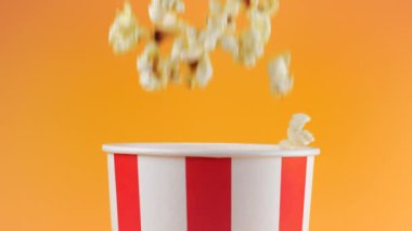 Patlamış mısır taneleri şeftali arka planda izole edilmiş kırmızı ve beyaz çizgili kovaya düşer. Atıştırmalık film, fast food kafe tatlı aperatif. Yavaş çekim.