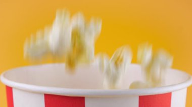 Patlamış mısır taneleri şeftali arka planda izole edilmiş kırmızı ve beyaz çizgili kovaya düşer. Atıştırmalık film, fast food kafe tatlı aperatif. Yavaş çekim.