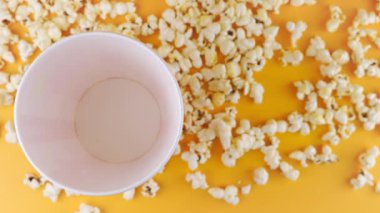 Patlamış mısır taneleri şeftali arka planda izole edilmiş kırmızı ve beyaz çizgili kovaya düşer. Atıştırmalık film, fast food kafe tatlı aperatif. Üst Manzara. Yavaş çekim.