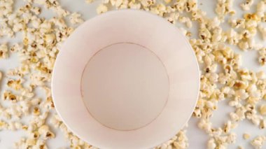 Patlamış mısır taneleri beyaz arka planda izole edilmiş kırmızı ve beyaz çizgili kovaya düşüyor. Atıştırmalık film, fast food kafe tatlı aperatif. Ağır çekim. Üst görünüm.