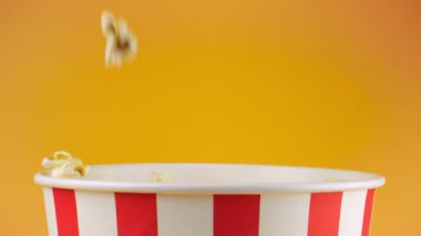 Patlamış mısır taneleri şeftali arka planda izole edilmiş kırmızı ve beyaz çizgili kovaya düşer. Atıştırmalık film, fast food kafe tatlı aperatif. Yavaş çekim.