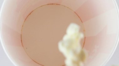 Patlamış mısır taneleri beyaz arka planda izole edilmiş kırmızı ve beyaz çizgili kovaya düşüyor. Atıştırmalık film, fast food kafe tatlı aperatif. Ağır çekim. Üst görünüm.